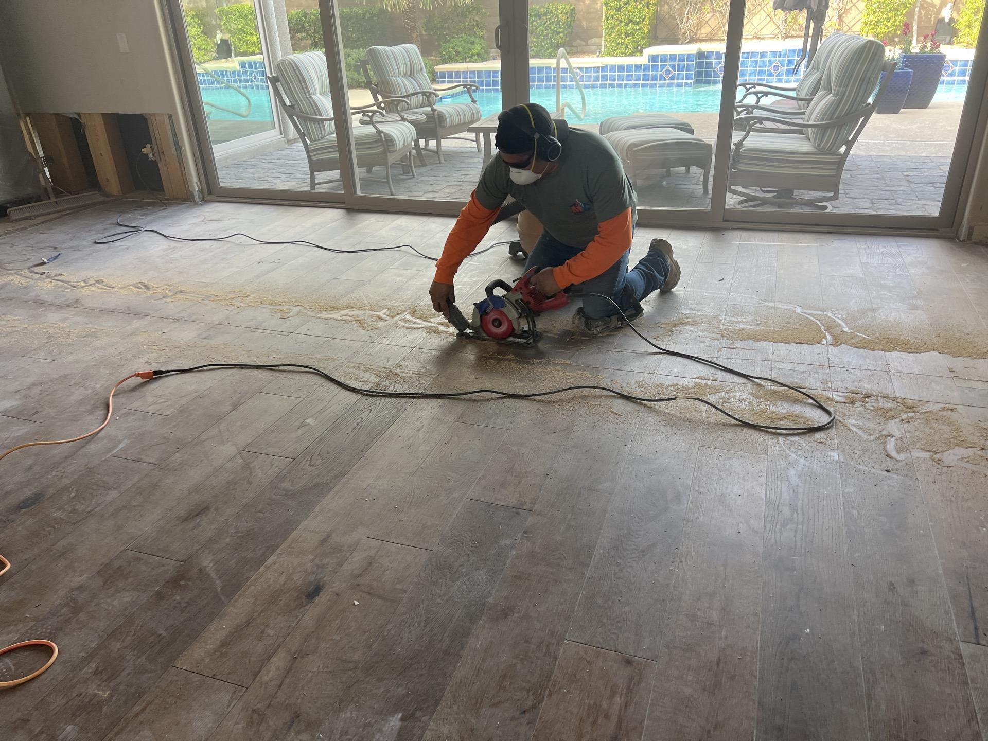 Technician cutting into water-damaged hardwood flooring during a water damage restoration project near a poolside patio in Las Vegas