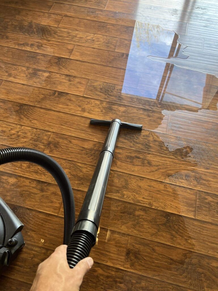 Technician extracting standing water from hardwood floor using a wet vacuum