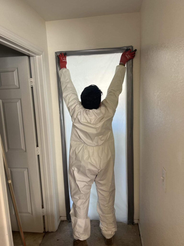 Technician in PPE installing a plastic doorway containment with tape to isolate a water-damaged area in a Las Vegas home.
